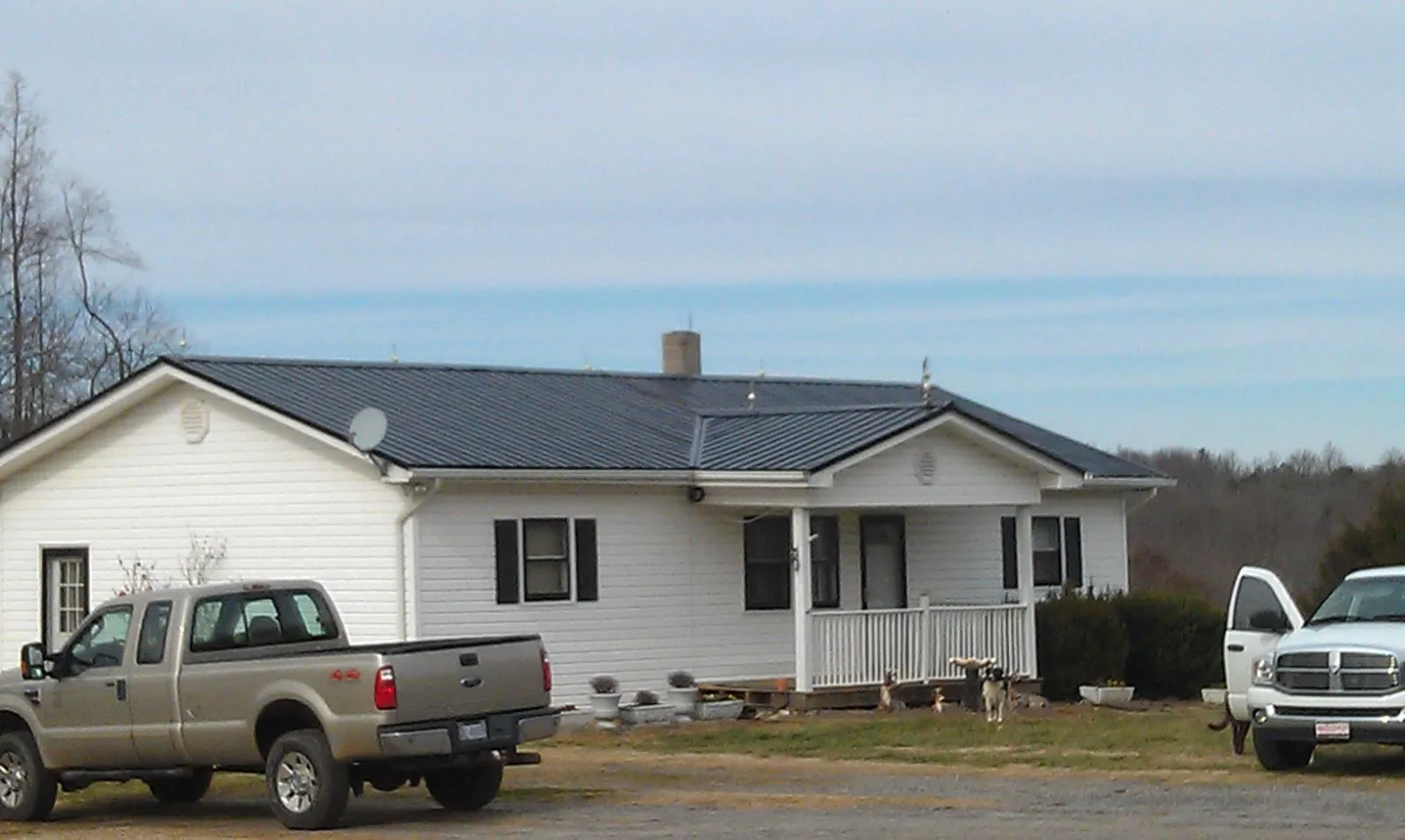 Finished dark metal roof on a white ranch home with work trucks parked in Gloucester