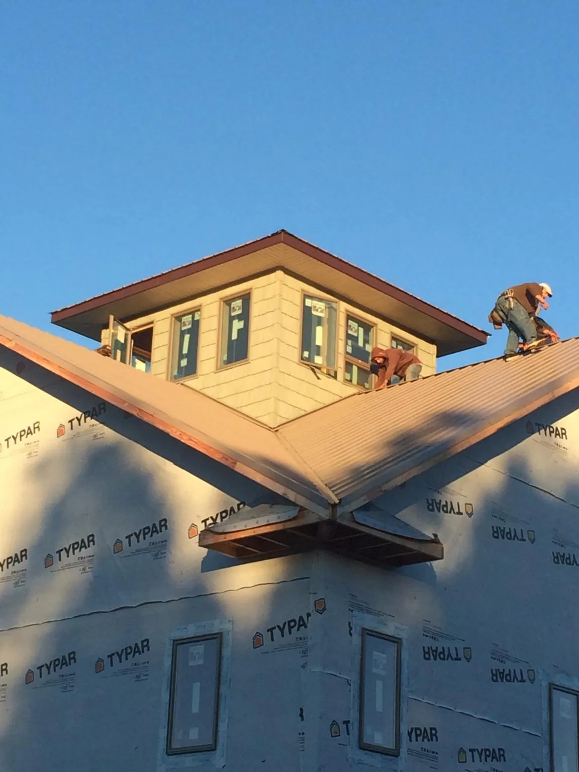 Roofers working around a rooftop cupola on a new metal roof at sunset — Roof Waterproofing in Gloucester by Roofing Brothers